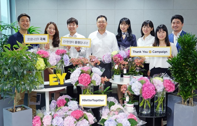 EY한영 박용근 대표이사(왼쪽 네번째)가 ’땡큐 스마일 캠페인’을 통해 주변 동료들로부터 꽃을 선물받은 EY한영 임직원들과 함께 코로나19 극복의 메시지를 담은 플래카드를 들고 기념촬영을 하고 있다.