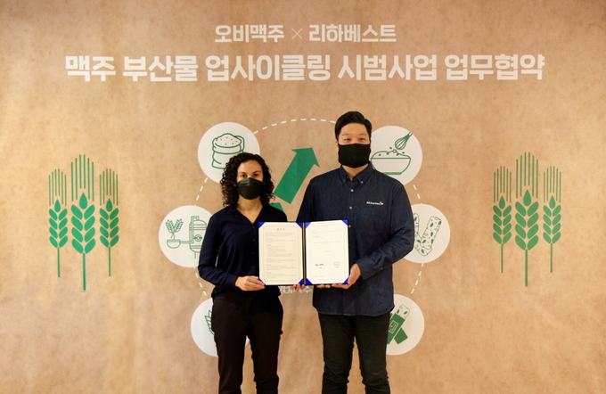 오비맥주 구매/지속가능경영 부문 나탈리 보르헤스 부사장(왼쪽)과 리하베스트 민명준 대표(오른쪽)가 맥주 부산물 업사이클링 사업을 위한 상생 협약을 맺고 기념촬영을 하고 있다.