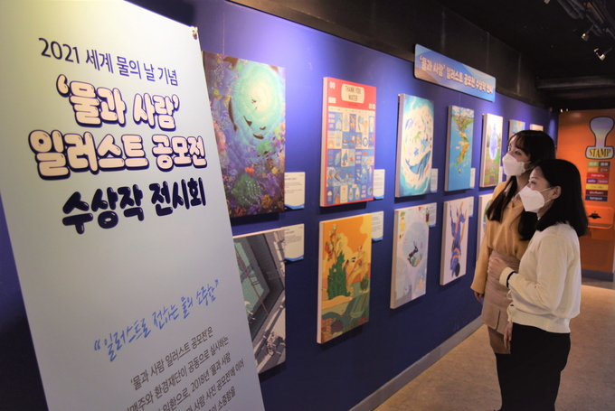 코엑스 아쿠아리움을 찾은 관람객들이 '물과 사람' 일러스트 공모전 수상작을 감상하고 있다.(사진=오비맥주)