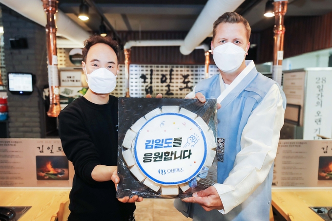 한복을 입은 오비맥주 배하준 대표(오른쪽)가 강남구 삼성동 인근 음식점을 방문해 응원 메시지가 담긴 떡 케이크를 전달하고 있다.