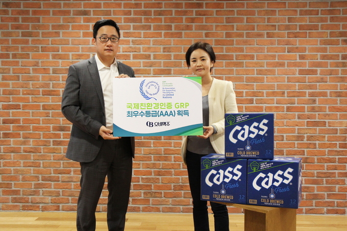 구자범 오비맥주 정책홍보부문 부사장(왼쪽)이 사회공헌팀 이은아 부장과 함께 오비맥주 GRP 인증 최우수등급 획득을 기념해 100% 재생용지로 제작한 카스 병맥주 상자 앞에서 사진을 찍고 있다.