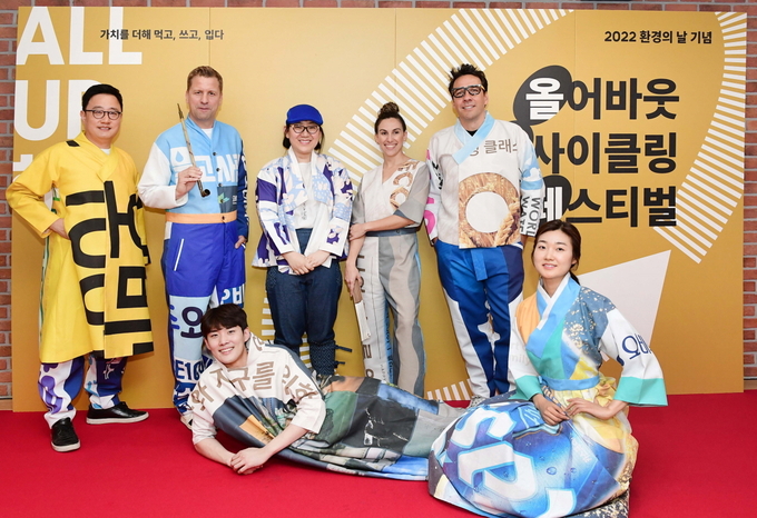 (뒷줄 왼쪽부터) 정책홍보부문 구자범 수석부사장, 배하준 대표이사, 다시곰 이승주 디자이너, 구매부문 나탈리 부사장, 마케팅부문 알렉스 부사장이 현수막으로 제작한 모던한복을 입고 기념사진을 찍고 있다 (사진=오비맥주)